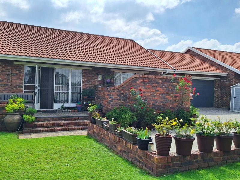 A well-maintained face-brick house featuring a terracotta tiled roof, paved driveway, integrated garage, and a charming front garden with a brick-walled patio area.