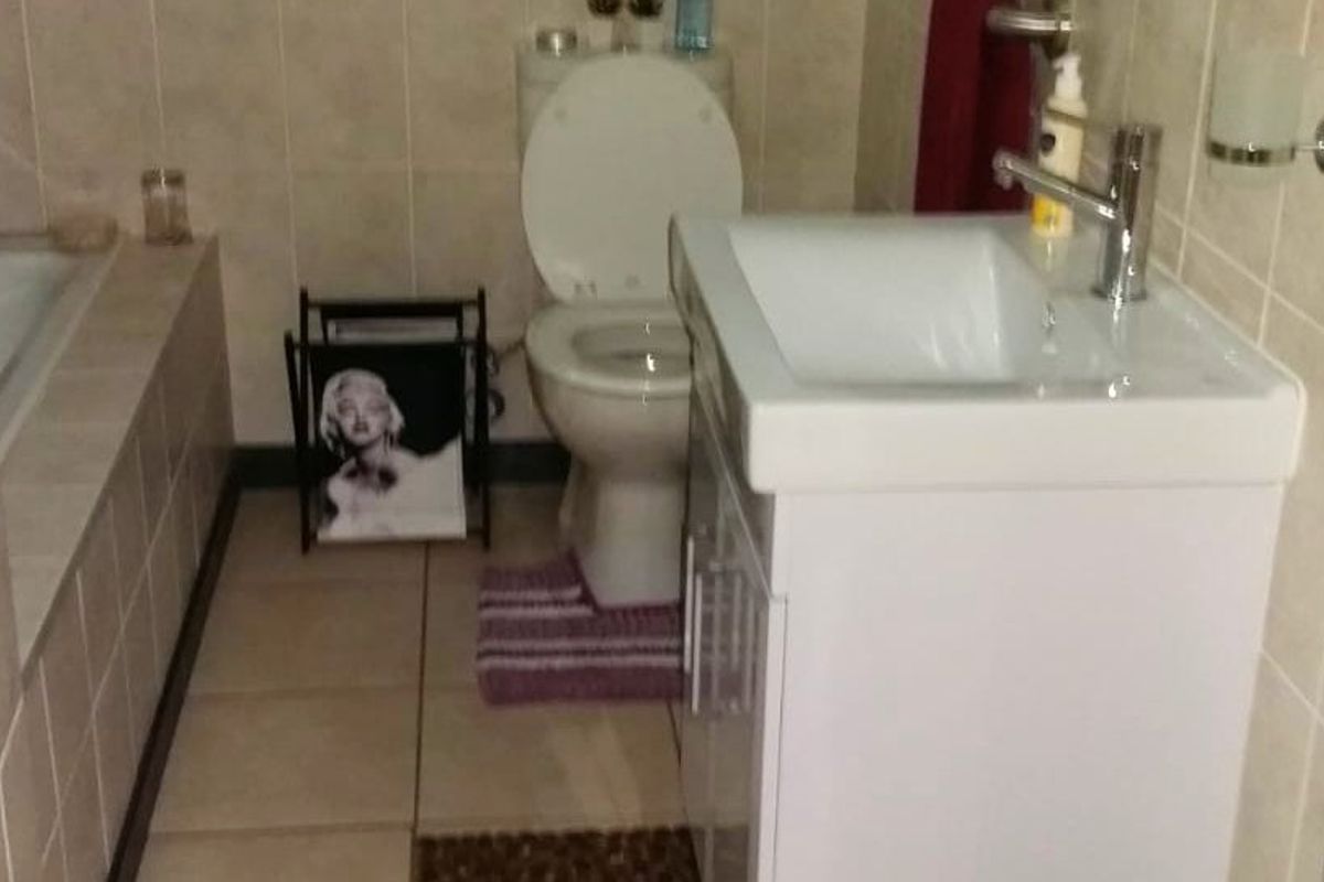 A functional bathroom featuring tiled walls and flooring, a built-in bathtub, a standard toilet, and a modern vanity basin with a chrome mixer tap.