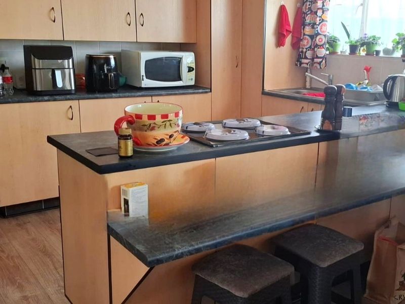 A functional kitchen featuring light wood-tone cabinetry, dark laminate countertops, a built-in hob, and a stainless steel sink with a breakfast bar area.