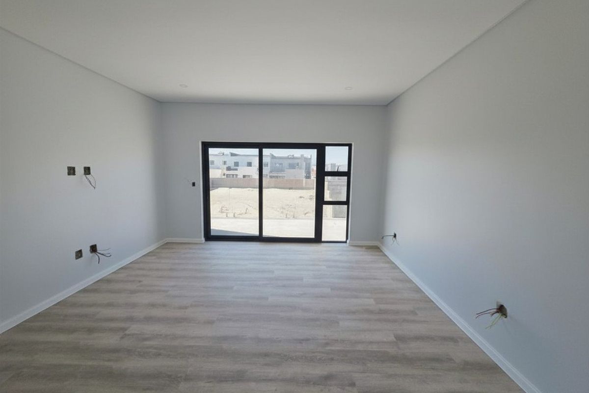 A bright, empty living room featuring modern light-toned laminate flooring and large black-framed sliding glass doors leading to an outdoor area.