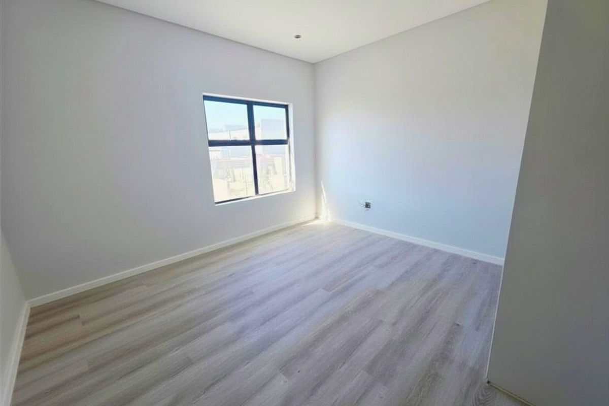 A bright, empty bedroom featuring modern light-toned wood-look flooring and neutral wall finishes, offering a clean and versatile space.