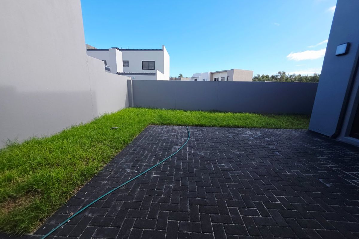 A private rear garden featuring a paved patio area and a well-maintained lawn, enclosed by modern boundary walls.