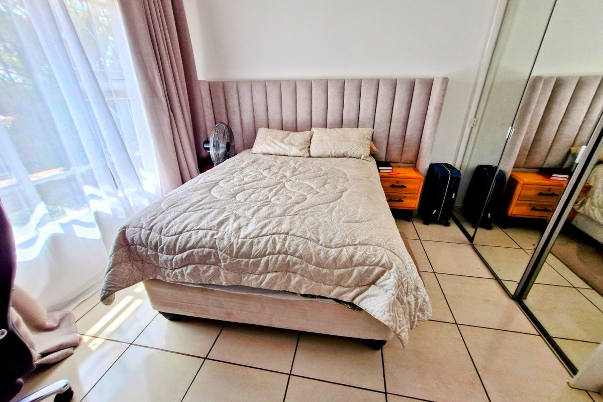 A bedroom featuring tiled flooring, a built-in wardrobe with mirrored doors, and a sliding glass door providing natural light.