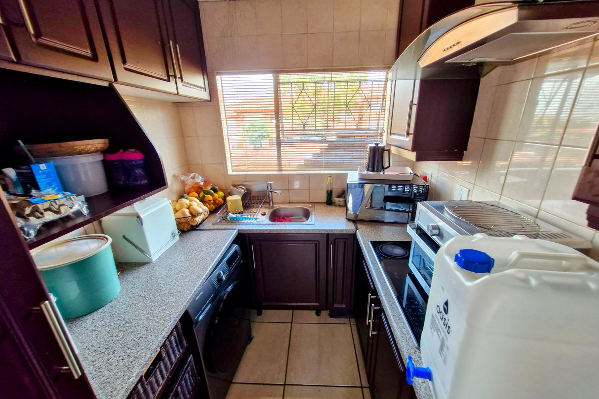 Compact kitchen featuring dark wood cabinetry, laminate countertops, ceramic tile backsplash, and integrated cooking appliances in a functional galley layout.