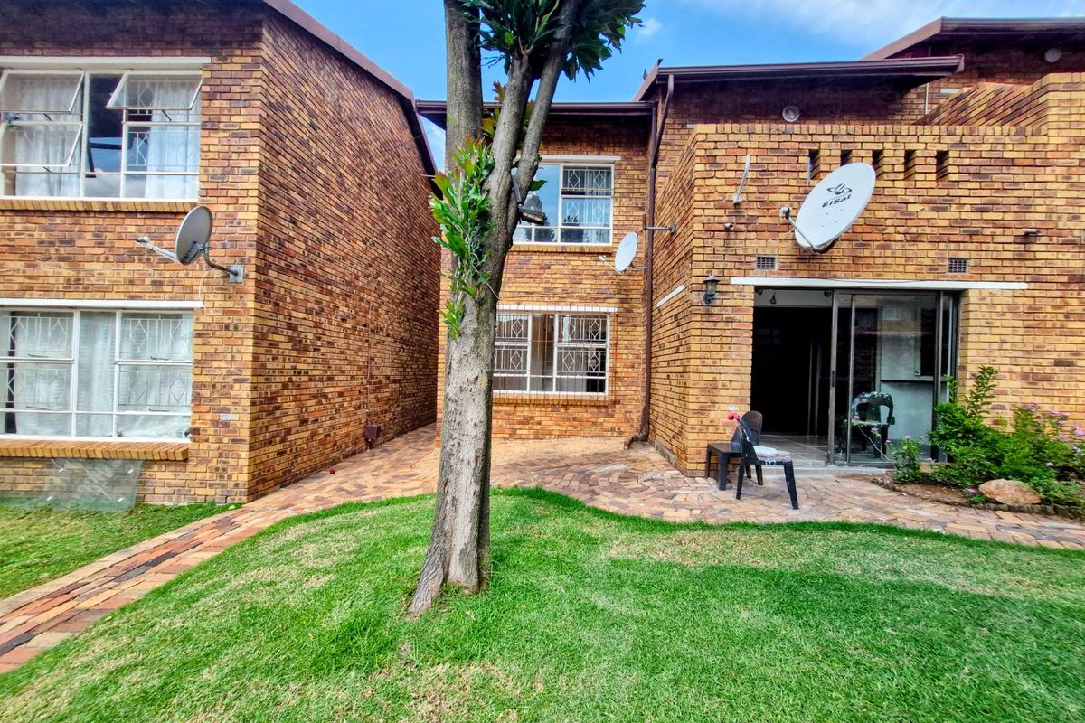 Rear view of a face brick townhouse featuring a paved patio area, lawn, and sliding door access to the interior.
