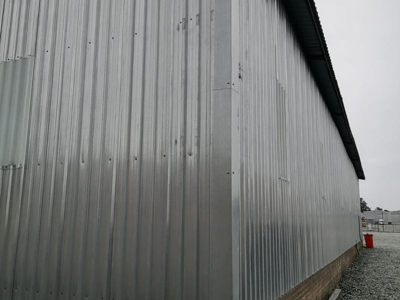 Exterior view of an industrial building featuring corrugated metal cladding over a brick base foundation.