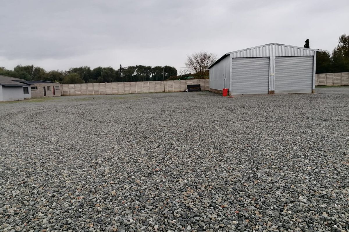 Spacious industrial yard featuring a gravel surface, secure precast concrete perimeter walling, and a double roller shutter garage unit.