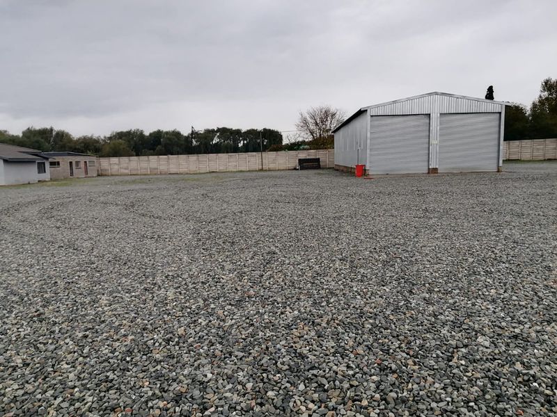 Spacious industrial yard featuring a gravel surface, secure precast concrete perimeter walling, and a double roller shutter garage unit.