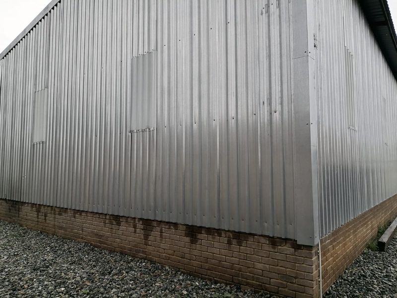 Exterior view of an industrial building featuring corrugated metal cladding over a brick plinth base with gravel ground surfacing.
