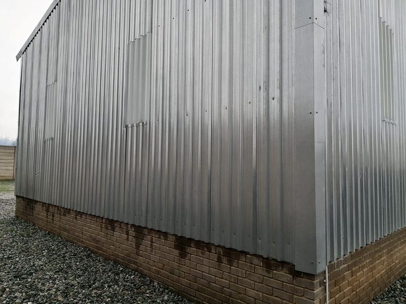Exterior view of an industrial building featuring corrugated metal wall cladding over a brick plinth base with gravel ground surfacing.