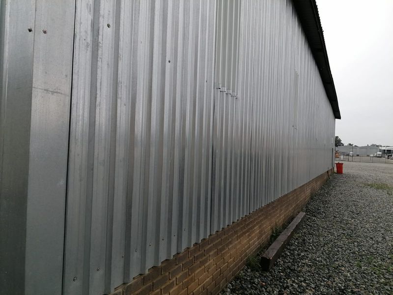 Side elevation of an industrial building featuring corrugated metal cladding over a brick base with a gravel perimeter.