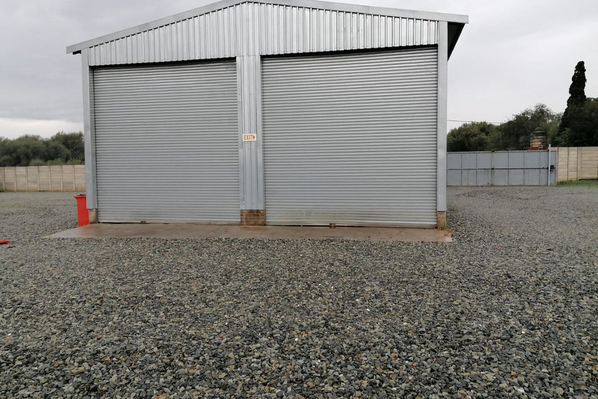 A detached industrial garage building featuring double roller shutter doors, set on a gravel yard with a concrete apron.