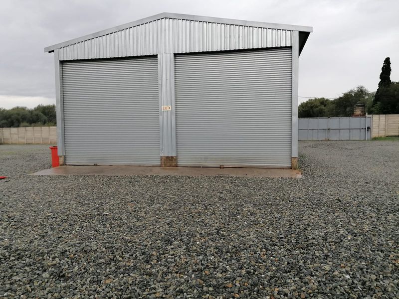 A detached industrial garage building featuring double roller shutter doors, set on a gravel yard with a concrete apron.