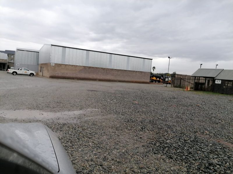 Industrial property exterior featuring a large gravel yard and corrugated metal warehouse structures.