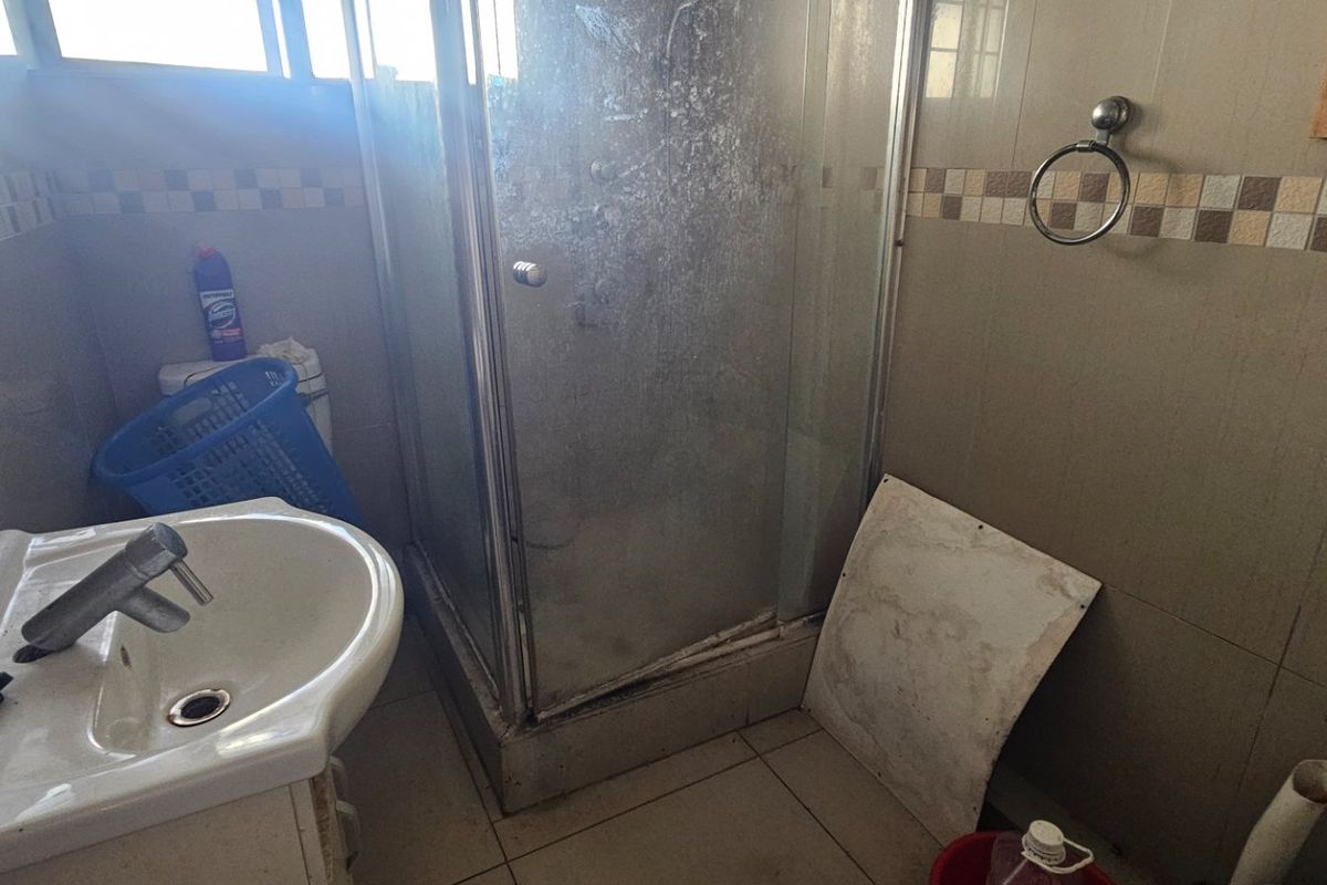 A dated bathroom featuring a shower enclosure and pedestal basin, currently requiring significant maintenance and cosmetic updates to restore functionality and appeal.