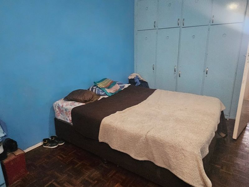 Bedroom featuring built-in cupboards and parquet flooring, with an adjacent bathroom visible through the doorway.