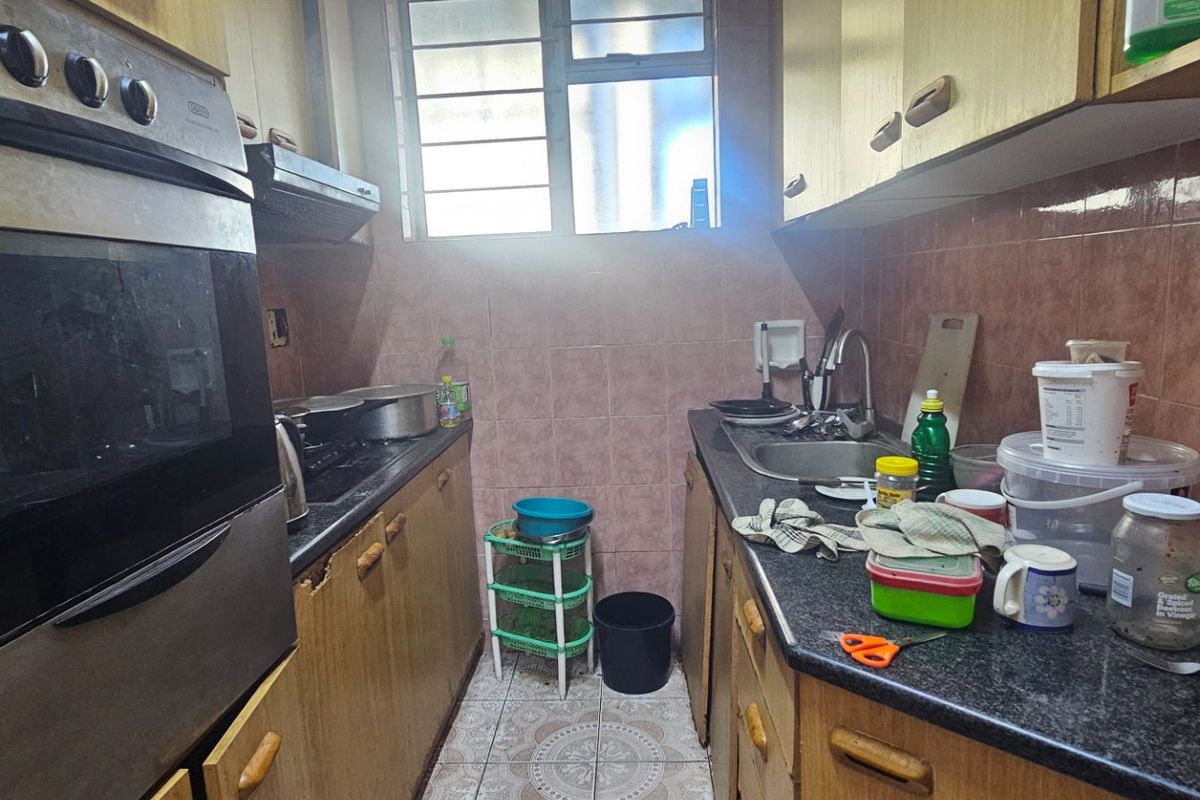 A compact galley-style kitchen featuring built-in oven, hob, extractor fan, granite countertops, and tiled backsplash, offering a functional layout with dated cabinetry.