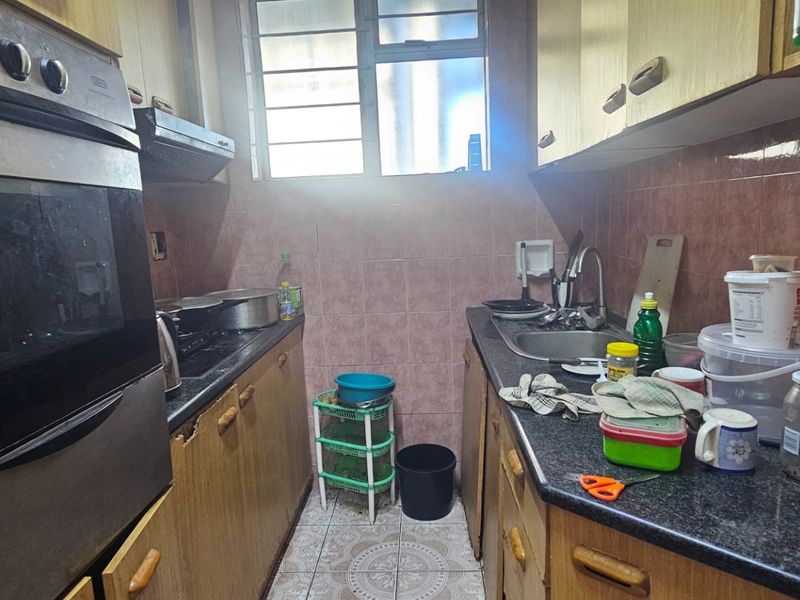 A compact galley-style kitchen featuring built-in oven, hob, extractor fan, granite countertops, and tiled backsplash, offering a functional layout with dated cabinetry.