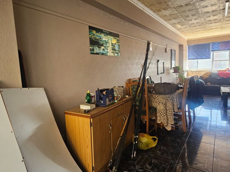 An open-plan living and dining area featuring tiled flooring and decorative ceiling tiles, offering a spacious layout with natural light from large windows.