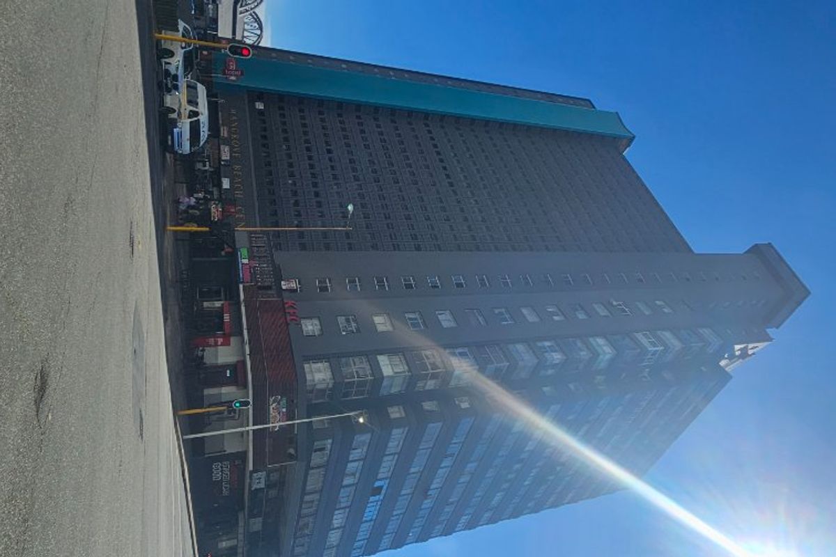 A low-angle street view of a high-rise apartment building featuring commercial retail space on the ground level.