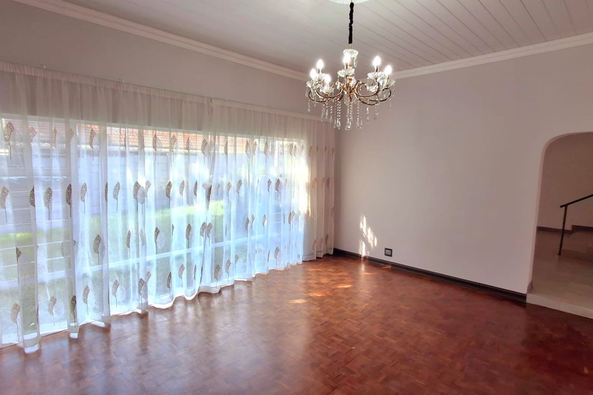 Spacious living room featuring classic parquet flooring, a decorative tongue and groove ceiling, and an elegant crystal chandelier, leading to an arched hallway.