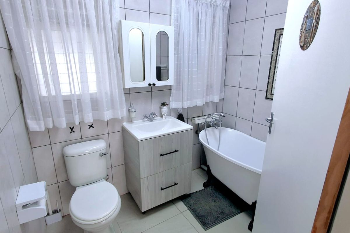 A clean, functional bathroom featuring a classic freestanding bathtub, a modern vanity unit with integrated basin, and neutral wall-to-floor tiling.