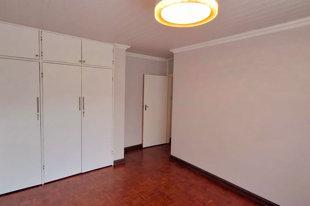 A clean, empty bedroom featuring warm parquet flooring, built-in cupboards with overhead storage, and a classic timber ceiling.