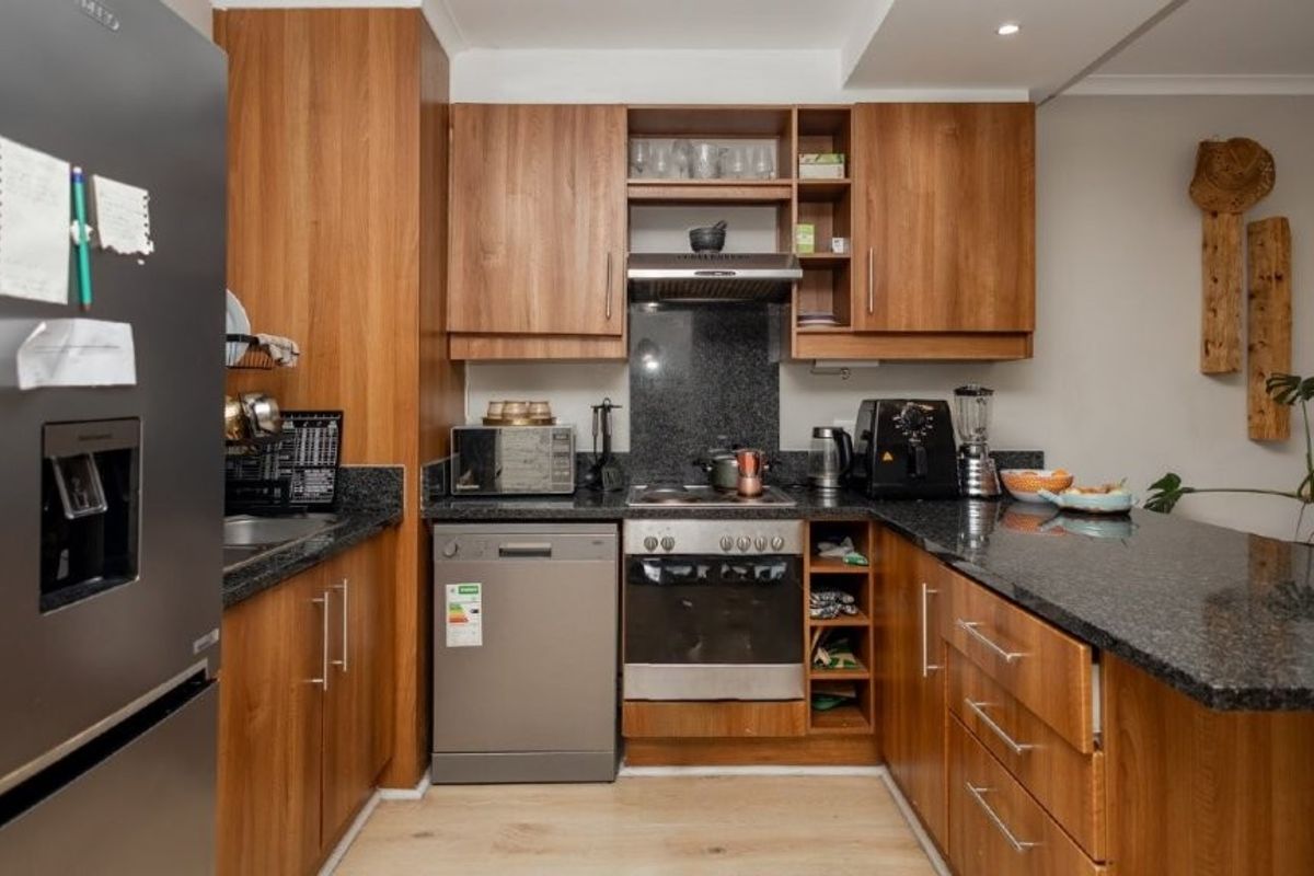 Compact kitchen featuring wood-finish cabinetry, granite countertops, a built-in oven, extractor fan, and integrated dishwasher space.
