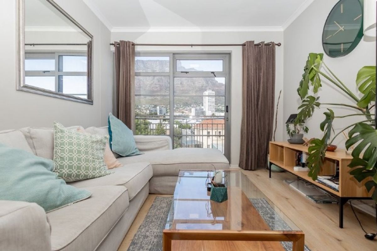 A bright living room featuring light wood flooring, neutral walls, and a sliding glass door that opens to a balcony with mountain views.