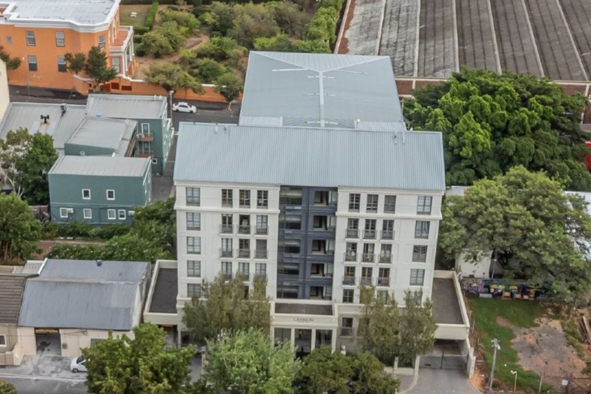 Aerial view of a multi-story apartment building featuring a metal roof, modern facade, and surrounding urban landscaping.