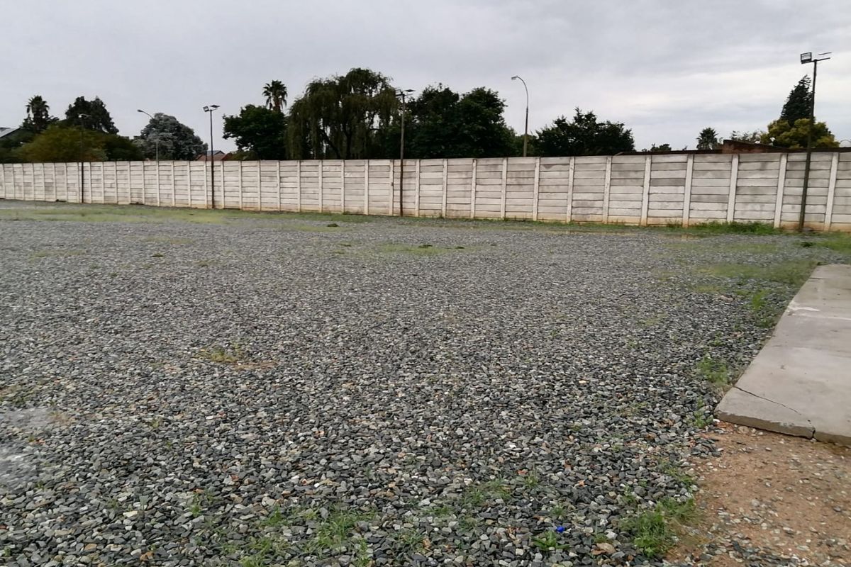 A large, open industrial yard featuring a gravel surface, enclosed by a precast concrete boundary wall with installed floodlights.