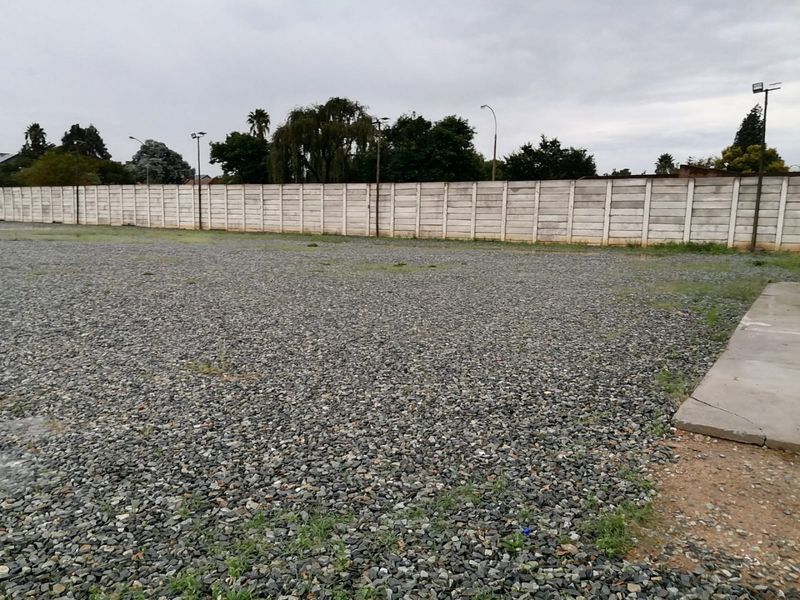 A large, open industrial yard featuring a gravel surface, enclosed by a precast concrete boundary wall with installed floodlights.