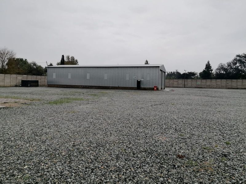 Industrial warehouse unit featuring corrugated metal cladding and a large gravel yard, enclosed by a secure precast concrete boundary wall.