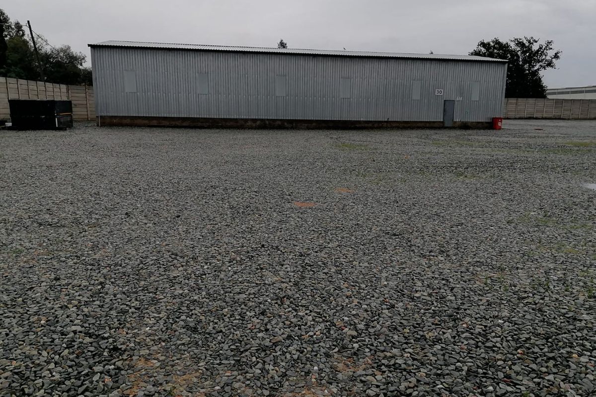 Industrial property featuring a large gravel yard and a corrugated metal warehouse structure with a secure perimeter wall.