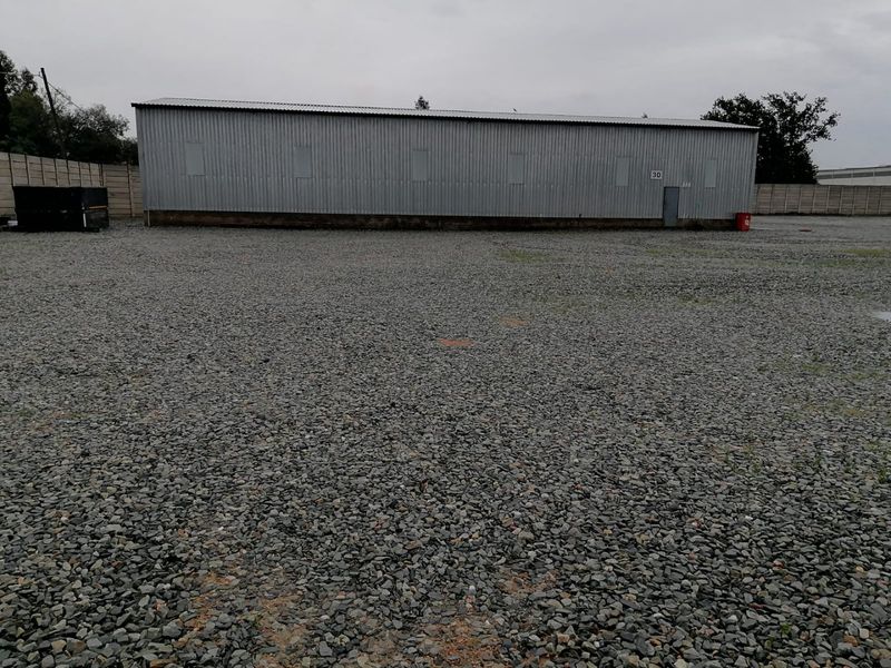Industrial property featuring a large gravel yard and a corrugated metal warehouse structure with a secure perimeter wall.