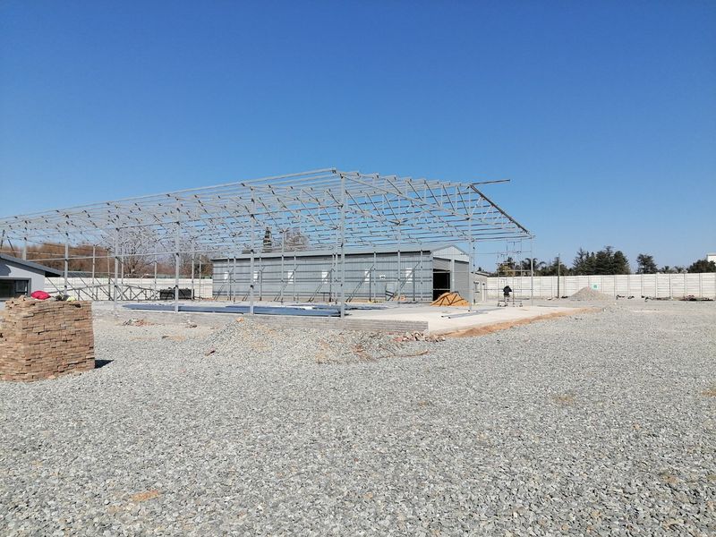 An industrial property under construction featuring a steel frame structure and concrete slab foundation on a gravel site.