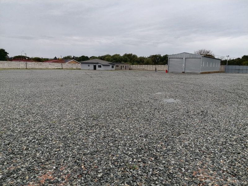 Expansive industrial yard featuring a gravel surface, secure precast boundary walling, and a functional metal shed with roller shutter access.