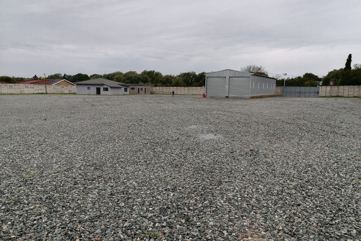 Expansive industrial property featuring a large gravel yard, a metal warehouse with roller shutter doors, and secure perimeter boundary walling.