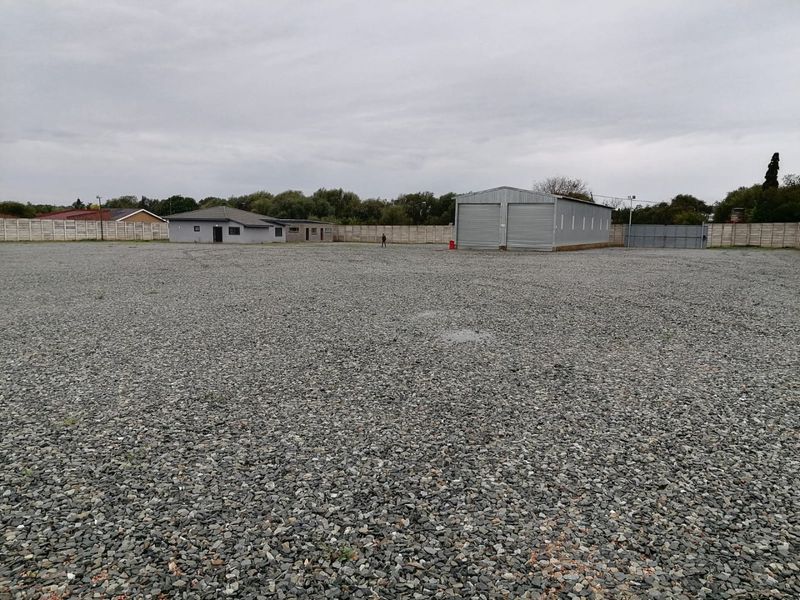 Expansive industrial property featuring a large gravel yard, a metal warehouse with roller shutter doors, and secure perimeter boundary walling.