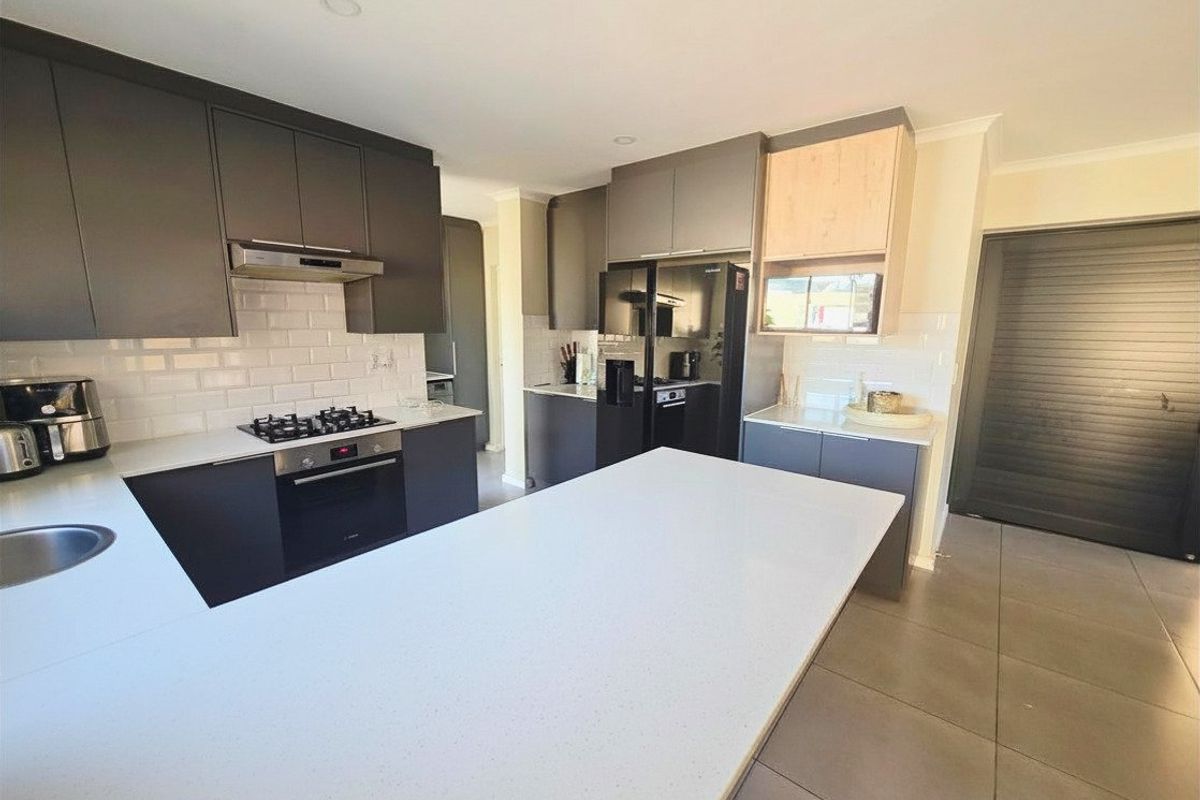Modern kitchen featuring dark cabinetry, quartz countertops, subway tile backsplash, a central island, and integrated appliances.