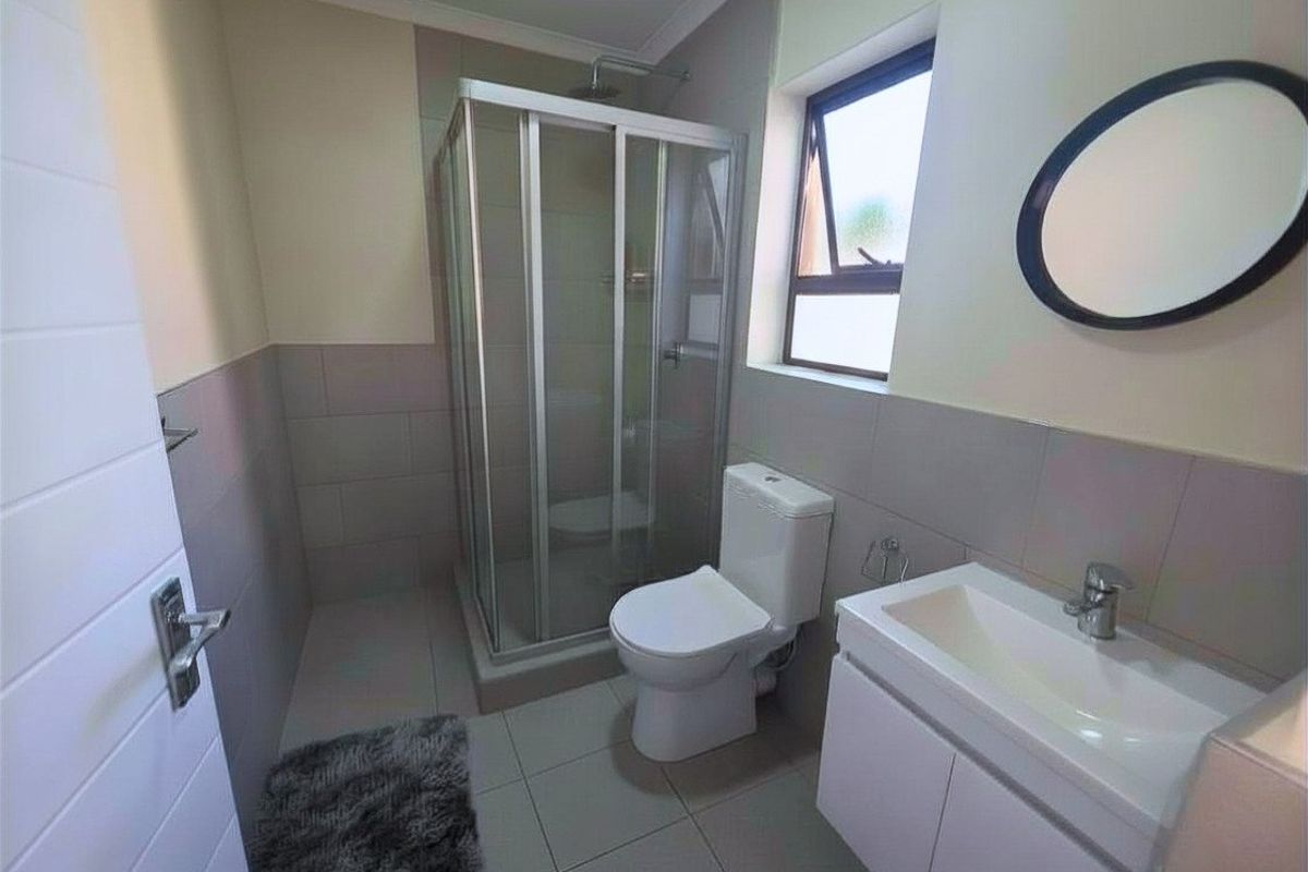 A clean, functional bathroom featuring a glass shower enclosure, a modern vanity basin, and neutral wall and floor tiling.