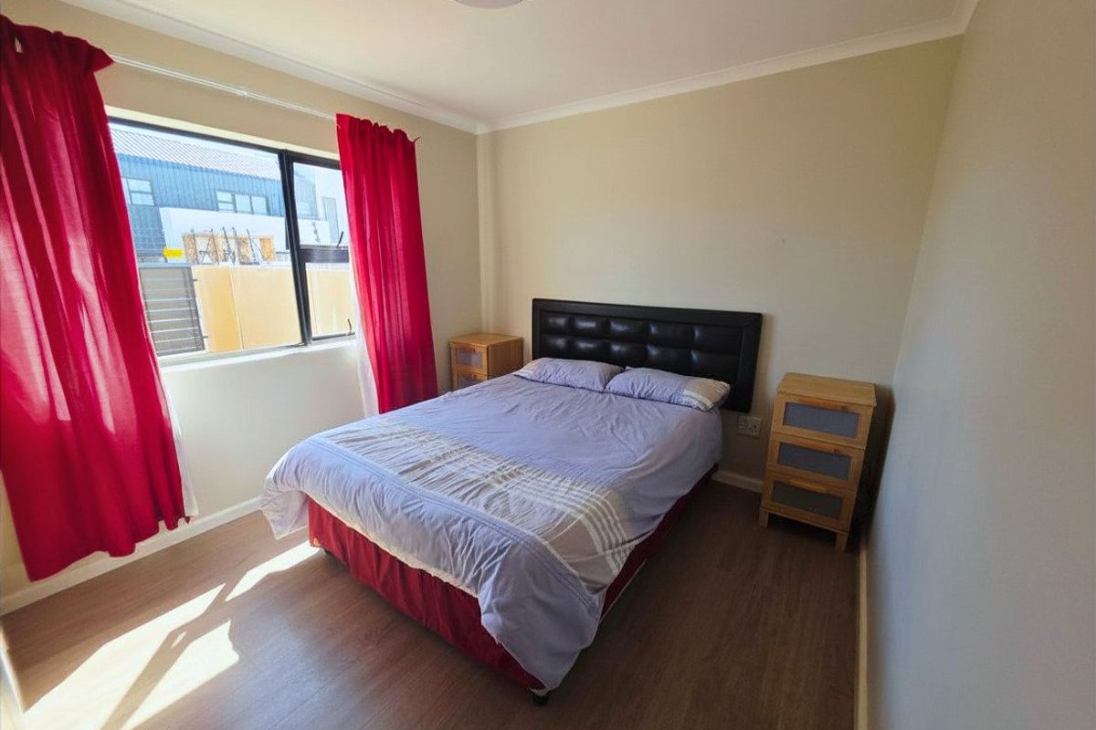 A functional bedroom featuring laminate flooring and a large window, providing a neutral base for potential interior design updates.