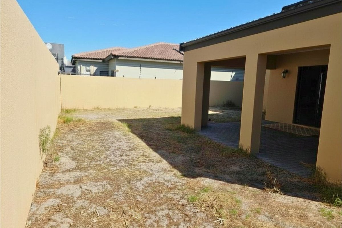 Rear exterior view featuring a covered patio area and a private garden space enclosed by high boundary walls.