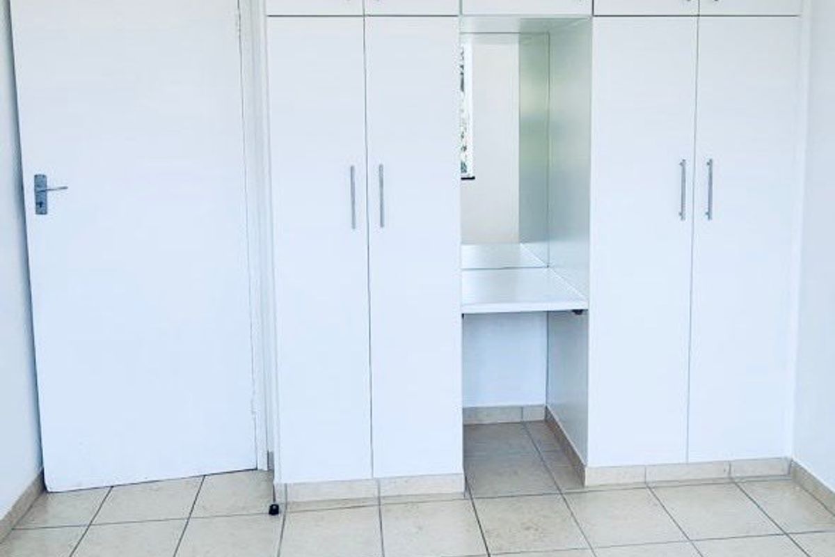 A clean, empty bedroom featuring white built-in cupboards with an integrated vanity station and neutral tiled flooring.