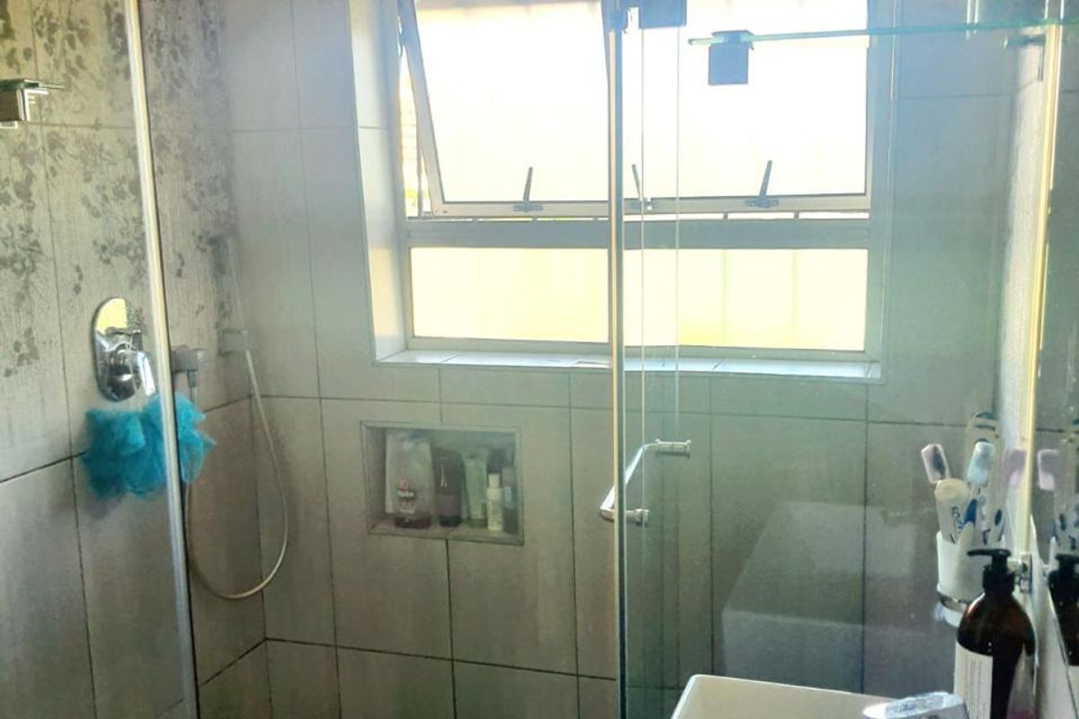 A functional bathroom featuring a walk-in shower with a glass screen, rain shower head, recessed niche, and a modern wall-mounted basin.