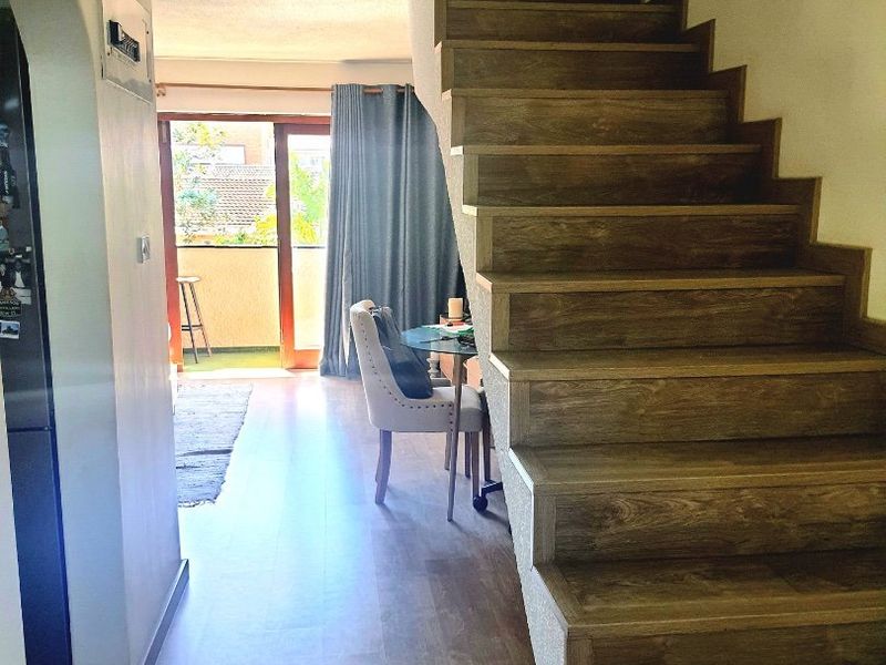 Interior hallway featuring a wooden staircase, laminate flooring, and a sliding glass door leading to a balcony area.