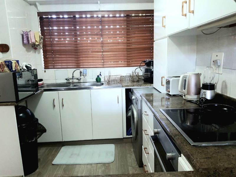 Functional kitchen featuring white cabinetry, granite countertops, integrated oven and hob, and a dedicated space for a washing machine.