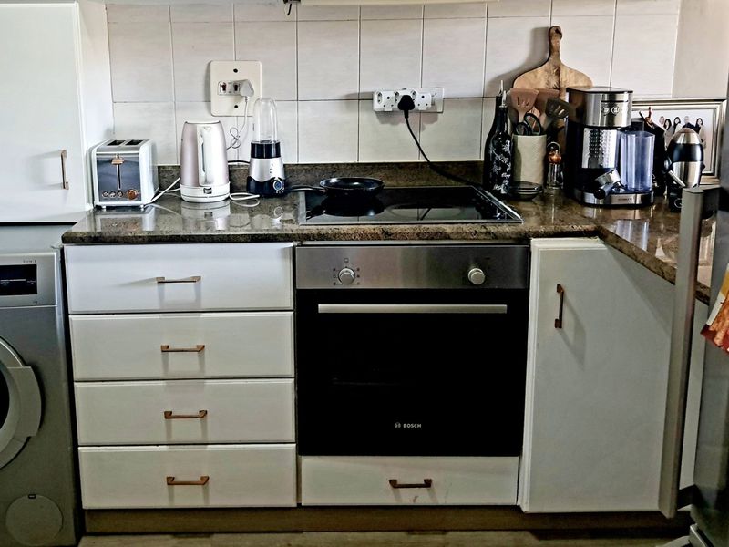 A functional kitchen area featuring granite countertops, a built-in Bosch oven, electric hob, tiled backsplash, and white cabinetry with integrated laundry appliance space.