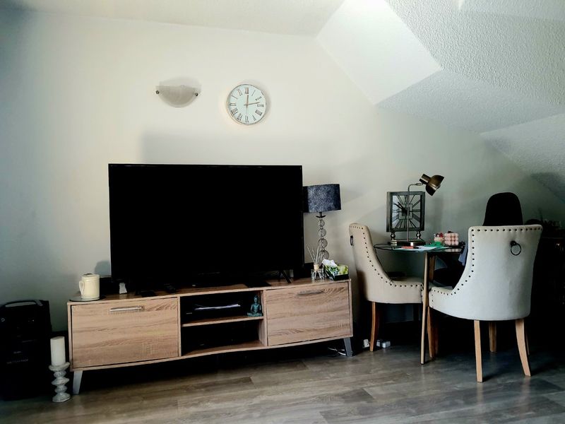 A living room area featuring sloped ceilings, laminate flooring, and a wall-mounted light fixture.