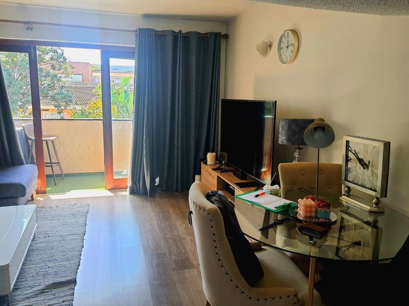 A living room area featuring laminate flooring and a sliding glass door providing access to a balcony.